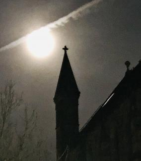 Vapour trail crossing moon above church