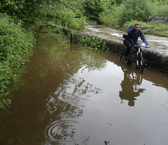 Man on bike riding through flooded footpath.